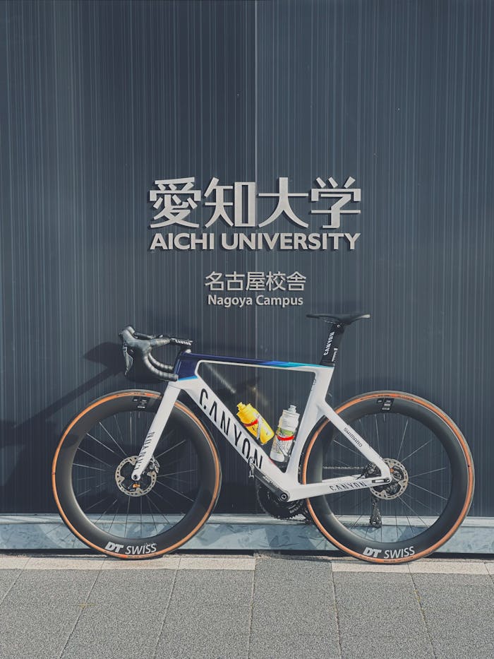 Canyon road bicycle parked at Aichi University's Nagoya Campus wall under clear daylight.
