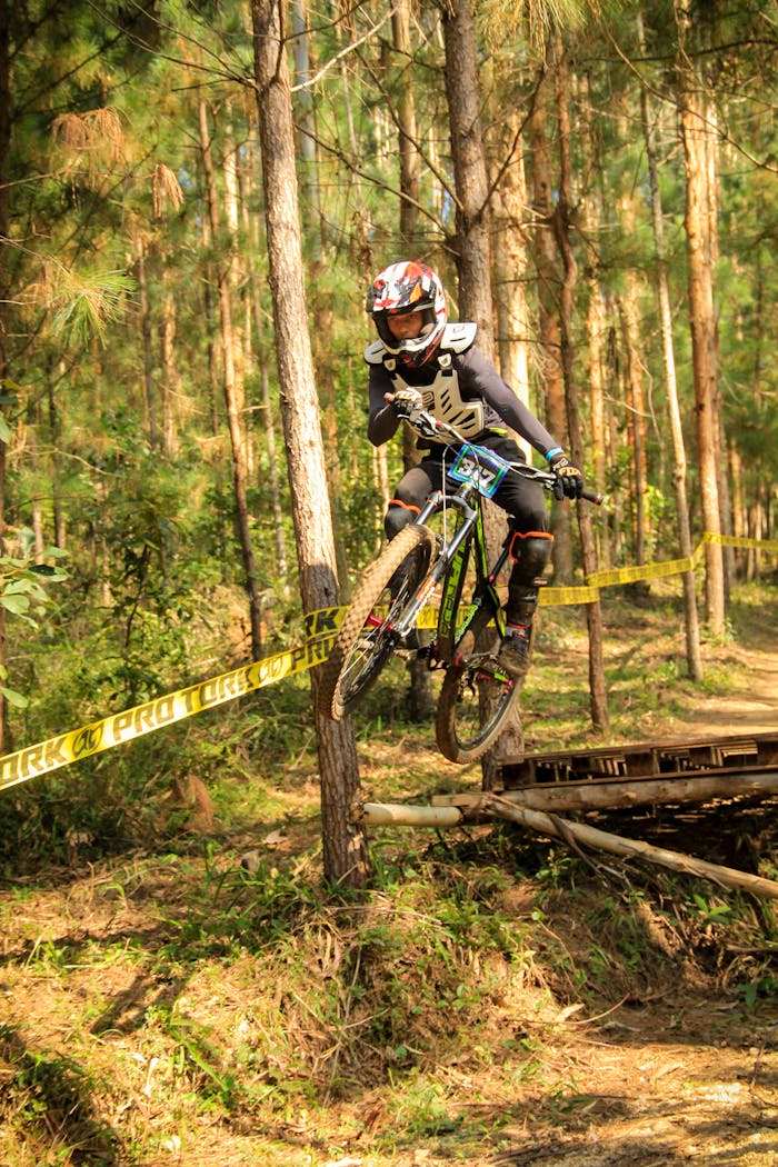Mountain biker jumps over obstacle on forest trail during race, showcasing skill and adrenaline.